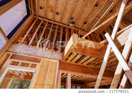 In new home under construction, trusses, post beams wood framework are being constructed out of unfinished house 117779351