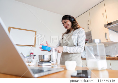 Smiling Woman Baking with Digital Recipe in Modern Kitchen Smiling Woman Baking with Digital Recipe in Modern Kitchen 117779416