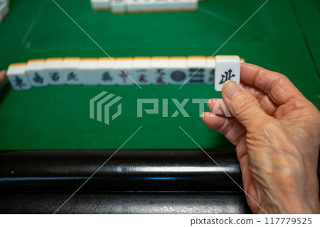 A senior holding a Kita tile as he plays mahjong on an electric mahjong table and tries to complete a kokushi musou 117779525