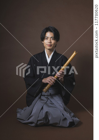 A man in a crested hakama playing a Japanese musical instrument 117780620