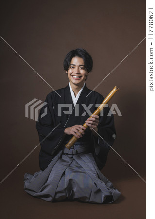 A man in a crested hakama playing a Japanese musical instrument A man in a crested hakama playing a Japanese musical instrument 117780621