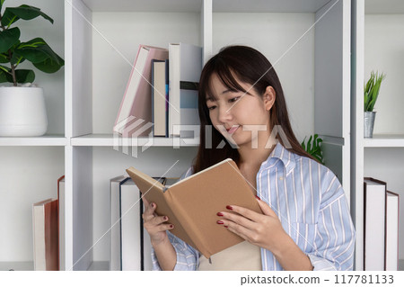 Young Woman Immersed in Reading Book in Home Library Young Woman Immersed in Reading Book in Home Library 117781133