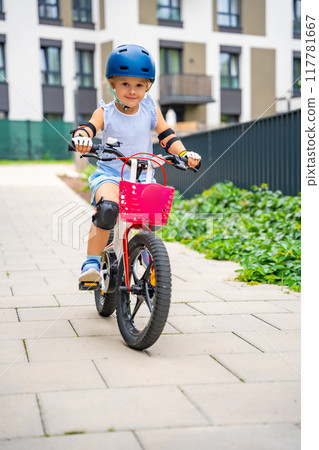 Little girl rides a two-wheeled bicycle Ii the courtyard of apartment buildings in summer, Europe 117781667