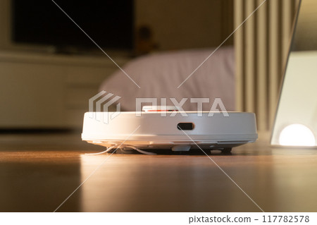 White robot vacuum cleaner cleaning floor in bedroom 117782578