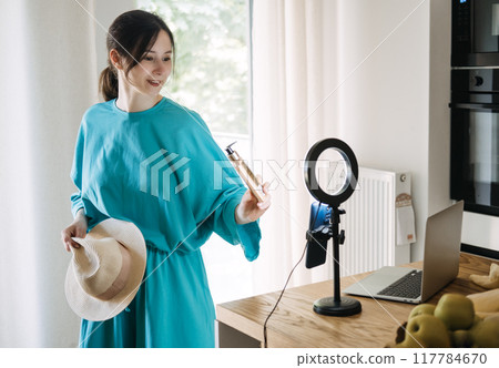Beauty blogger demonstrating skincare product with sunhat, content creation for social media, influencer marketing, summer skincare tips, online brand promotion. Beauty blogger demonstrating skincare product with sunhat, content creation for social media, influencer marketing, summer skincare tips, online brand promotion. 117784670