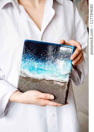 Close-up of person holding ocean-inspired resin art piece, showcasing detailed craftsmanship and unique design. Handmade coastal-themed home decor. 117784680