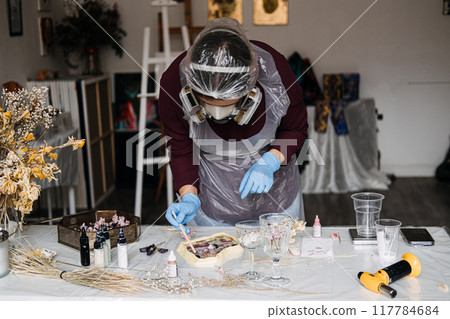 Craftsperson wearing safety gear while creating resin art with dried flowers. DIY home decor with focus on safety and sustainable materials. 117784684