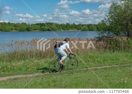 girl on a bicycle rides along a path along the coast overgrown with reeds girl on a bicycle rides along a path along the coast overgrown with reeds 117785488