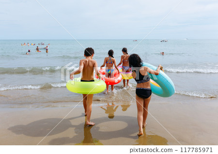 rear view of small group of children entering the sea with inflatable rings rear view of small group of children entering the sea with inflatable rings 117785971