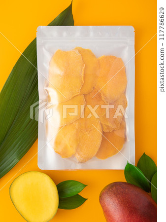 Large pack of dried mango slices with leaf and raw mango on yellow background.Macro 117786629