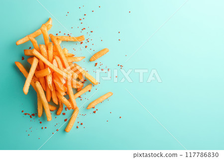 A vibrant pile of crispy golden fries sprinkled with seasoning on a turquoise background, perfect for food-related projects. 117786830