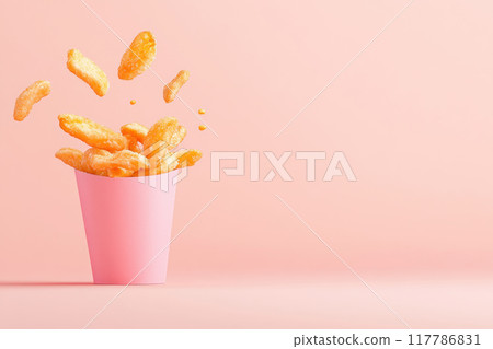 A vibrant pink cup filled with golden snacks, and some are playfully bouncing out, set against a soft pink background. 117786831