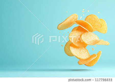 A vibrant splash of golden potato chips against a blue background, showcasing freshness and fun. Perfect for snack-related themes. 117786833