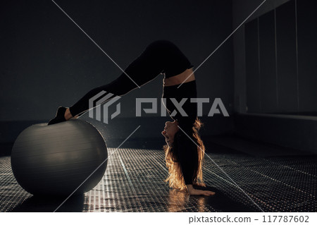 A determined young woman skillfully balances on an exercise ball in a modern fitness studio, showcasing her strength and flexibility, inspiring others to pursue their health and fitness goals 117787602