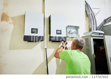 Man electrician installing solar panel system. Inspector making electrical wiring inverter and electric box. Concept of alternative and renewable energy. 117787885