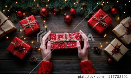 Hands gently holding a red gift surrounded by festive decorations and presents during Christmas 117788591