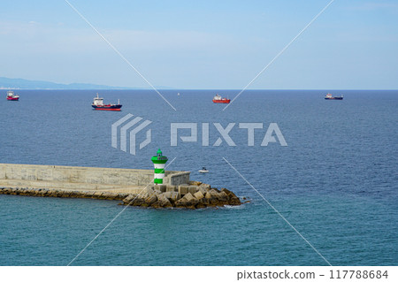Ship traffic near the port, concrete pier of the port with a small lighthouse in the foreground 117788684