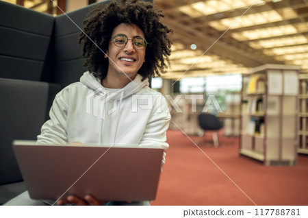 Young male student using laptop for remote studying preparing for seminars in library 117788781