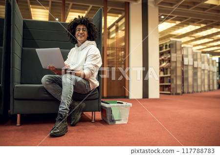 Man student working on his project while sitting in the educational establishment library Man student working on his project while sitting in the educational establishment library 117788783
