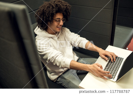 Man student working on his project while sitting in the educational establishment library Man student working on his project while sitting in the educational establishment library 117788787