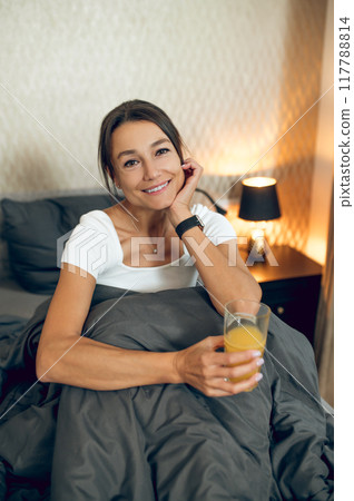 Smiling relaxed woman having orange juice in the morning after wake up Smiling relaxed woman having orange juice in the morning after wake up 117788814