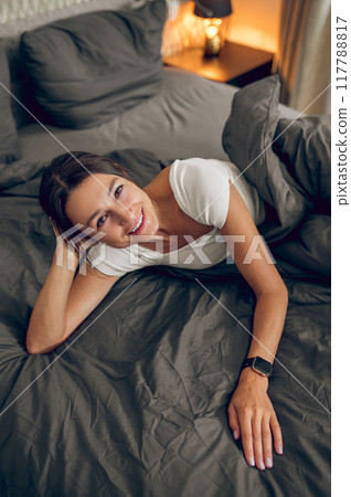 Dark-haired woman feeling relaxed in her bedroom in the morning Dark-haired woman feeling relaxed in her bedroom in the morning 117788817