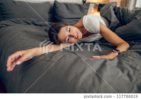 Dark-haired woman feeling relaxed in her bedroom in the morning Dark-haired woman feeling relaxed in her bedroom in the morning 117788819