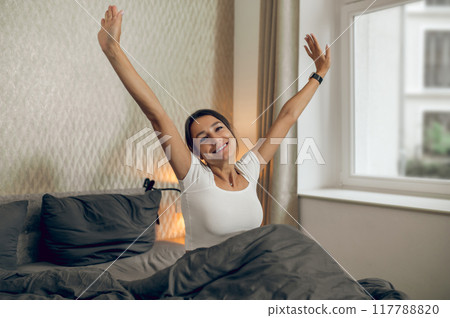 Dark-haired woman feeling relaxed in her bedroom in the morning Dark-haired woman feeling relaxed in her bedroom in the morning 117788820