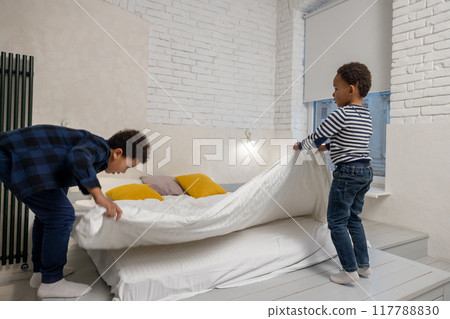 Siblings making bed together and fixing a flock bed Siblings making bed together and fixing a flock bed 117788830