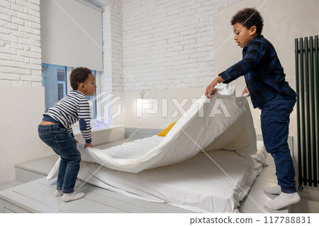 Siblings making bed together and fixing a flock bed Siblings making bed together and fixing a flock bed 117788831