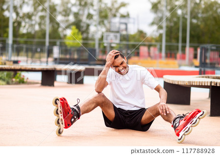 Young man learning riding the rollers and laughing while falling down 117788928