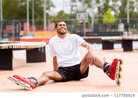 Young man learning riding the rollers and laughing while falling down 117788929