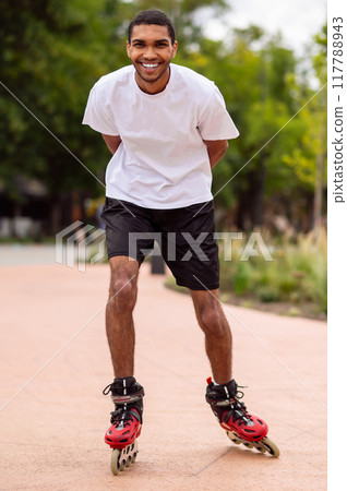 Tall dark-haired young man on rollers in the park having a ride Tall dark-haired young man on rollers in the park having a ride 117788943