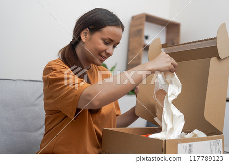 Wardrobe Happiness: A content woman, eager to explore her parcel, revels in the quality of her online fashion store finds. Wardrobe Happiness: A content woman, eager to explore her parcel, revels in the quality of her online fashion store finds. 117789123