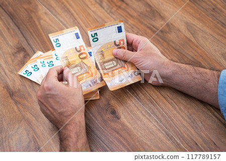 Hands managing 50 euro banknotes on a wooden table. Concept of currency handling, financial organization, and budgeting  117789157