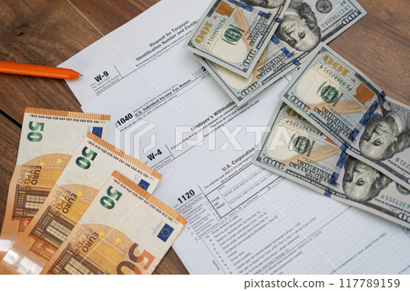 Tax forms with U.S. dollars and euros on a wooden table, featuring tax documents and currency. Financial concept for tax filing and preparation. Accounting and tax season essentials Tax forms with U.S. dollars and euros on a wooden table, featuring tax documents and currency. Financial concept for tax filing and preparation. Accounting and tax season essentials 117789159