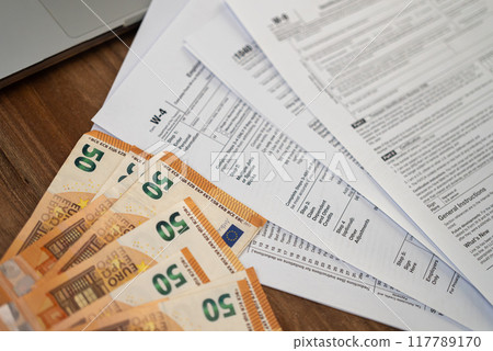 Tax forms and fifty-euro banknotes on a wooden desk. Financial management and international tax preparation concept. Suitable for accounting and finance-related themes  117789170