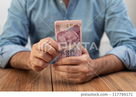 Man holding a stack of Turkish lira banknotes on a wooden table. Economic concept illustrating inflation and finance in Turkey.  117789171