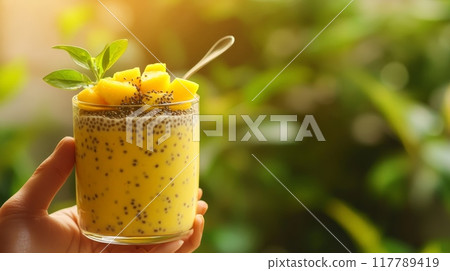 Mango chia pudding in a glass jar with fresh mango cubes against a green background. Tropical summer dessert. 117789419