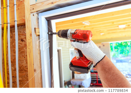 Installation of front door of new house is undertaken by carpenter using screwdriver Installation of front door of new house is undertaken by carpenter using screwdriver 117789834