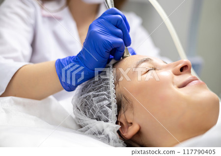Close-up side shot of a beautiful young woman on a facial derma pen micro-needling treatment at the beauty salon. 117790405