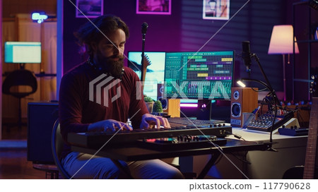Sound engineer playing electronic piano keyboard and recording sounds, using mixing console and daw software to create new tunes. Music industry specialist uses stereo tools at home studio. Camera A. 117790628