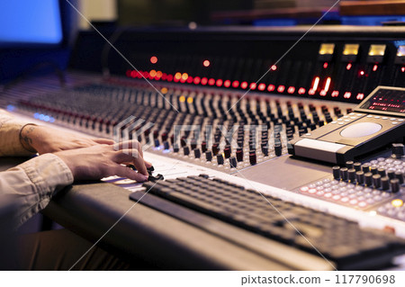 Audio engineer twisting pre amp knobs and switchers on panel board in control room, using mixing console for editing and mastering music. Professional skilled producer in music studio. 117790698