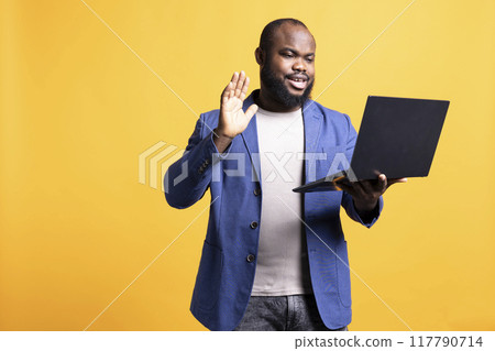 Teleworking executive discussing with coworkers during video conference meeting, studio background. Cheerful manager holding online video call with colleagues using laptop device 117790714