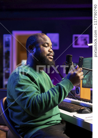 African american singer producer recording his new creation in home studio, singing a new track on microphone and edit it later in post production. New acoustic version song, stereo gear. 117790740