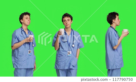 Medical assistant drinking cup of coffee before starting exam appointments in the morning, enjoying caffeine refreshment against greenscreen backdrop. Nurse drinks beverage. Camera B. Medical assistant drinking cup of coffee before starting exam appointments in the morning, enjoying caffeine refreshment against greenscreen backdrop. Nurse drinks beverage. Camera B. 117790750