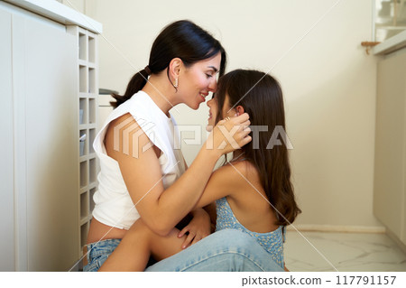 A joyful moment between a mother and daughter sharing a loving embrace at home in the afternoon light 117791157