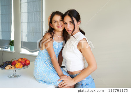 Mother and daughter posing together in a cozy kitchen with fresh fruit on the table Mother and daughter posing together in a cozy kitchen with fresh fruit on the table 117791175