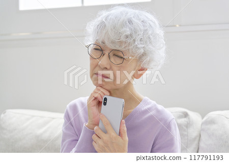 Senior woman thinking with smartphone in living room 117791193