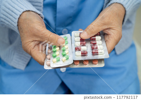 Asian senior woman patient holding antibiotics capsule pills  for treatment infection patient in hospital, Pharmacy drugstore concept. 117792117